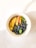 A bowl filled with a healthy mixture featuring slices of peach, fresh blueberries, chia seeds, and pumpkin seeds, garnished with a couple of green leaves. The bowl is set against a light background, creating a fresh and appetizing presentation.