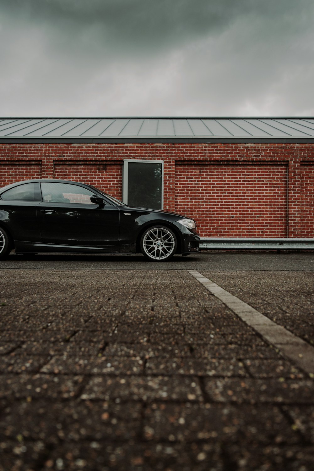 black coupe parked beside red brick wall