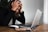 A person is sitting at a table with a laptop in front of them, holding their head in frustration. Glasses and a smartphone are also on the table, suggesting a work or study environment.