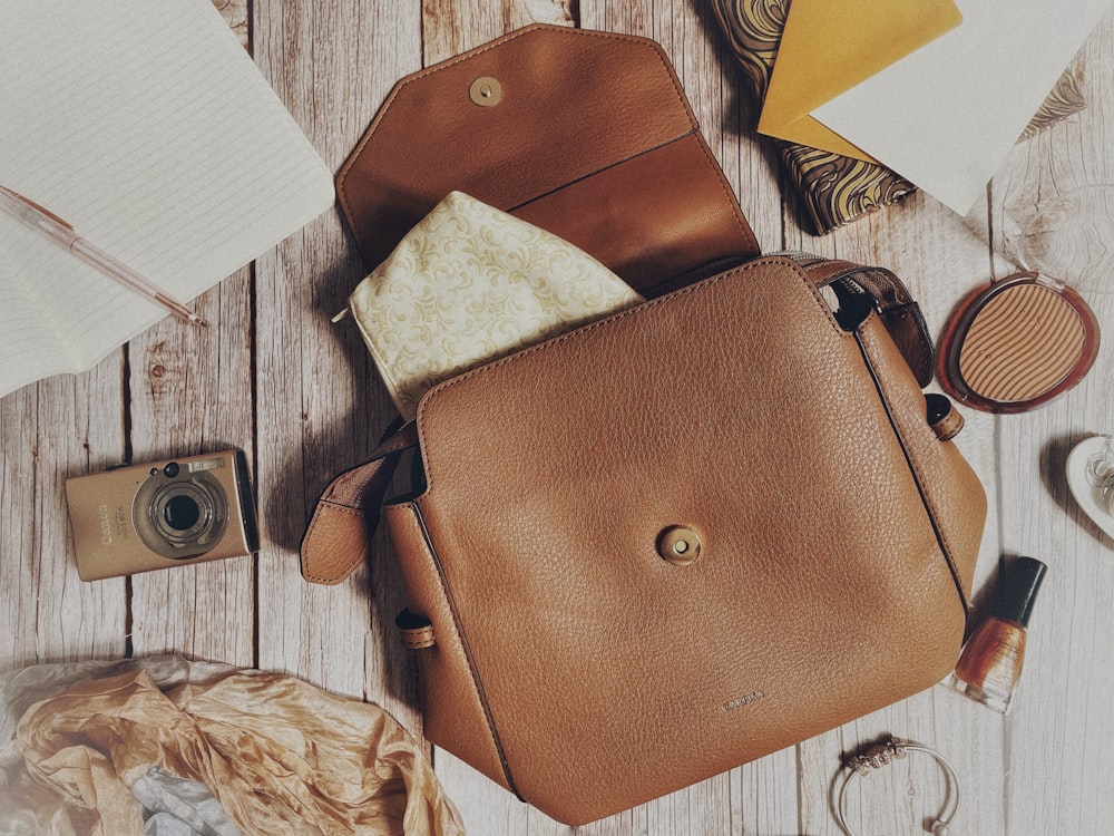 brown leather sling bag beside silver and gold camera
