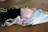 A collection of disposable face masks in different colors, including black, pink, and blue, placed on a wooden surface. The masks have white elastic ear loops.