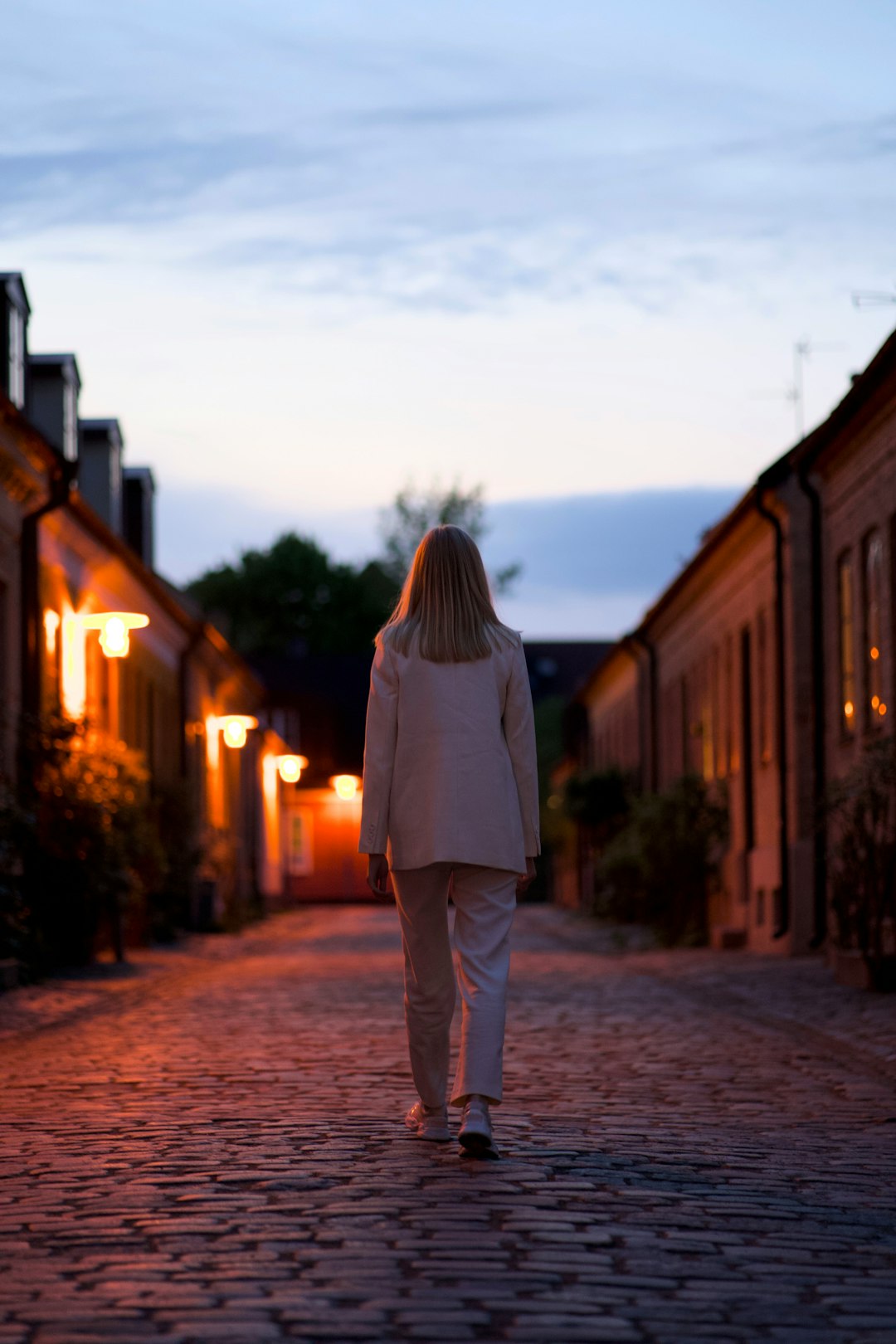 woman in white long sleeve shirt and gray pants standing on brown brick pathway during sunset