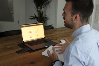 A friendly mentor answering questions at a desk with a laptop and notes.