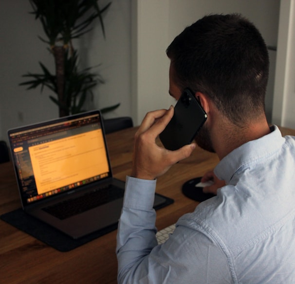 man in blue dress shirt holding black smartphone