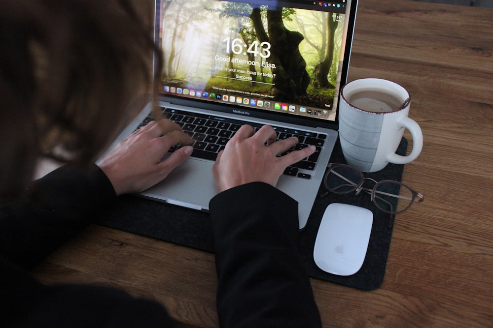Persona usando MacBook Pro en una mesa de madera marrón