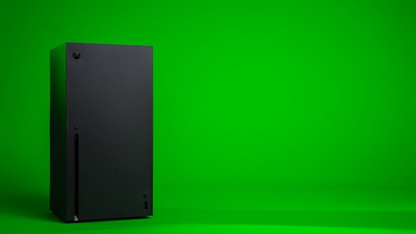 A black, rectangular gaming console stands upright against a vibrant green background. The console has a simple, sleek design with minimalistic features including a disc slot and a few buttons.