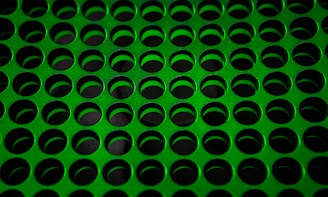 A pattern of evenly spaced, circular holes cut into a green perforated metal sheet, creating a uniform grid across the surface.