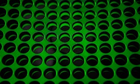 A pattern of evenly spaced, circular holes cut into a green perforated metal sheet, creating a uniform grid across the surface.