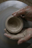 Close-up of a freshly thrown clay bowl on the wheel, hands shaping the rim.