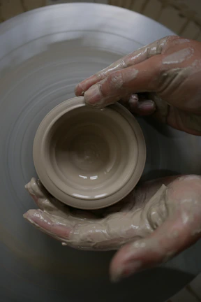 Close-up of a freshly thrown clay bowl on the wheel, hands shaping the rim.