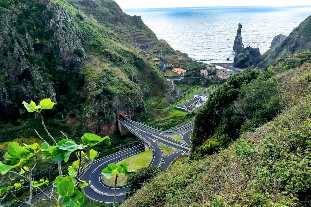 gray concrete road between green mountains and body of water during daytime