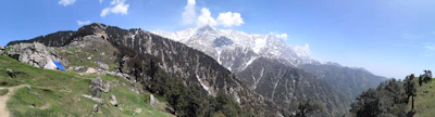 A panoramic view of snow-capped mountains in Himachal Pradesh with a luxury tent camp nestled among pine trees.