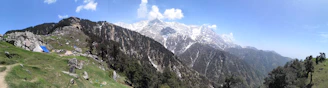 A panoramic view of snow-capped mountains in Himachal Pradesh with a luxury tent camp nestled among pine trees.