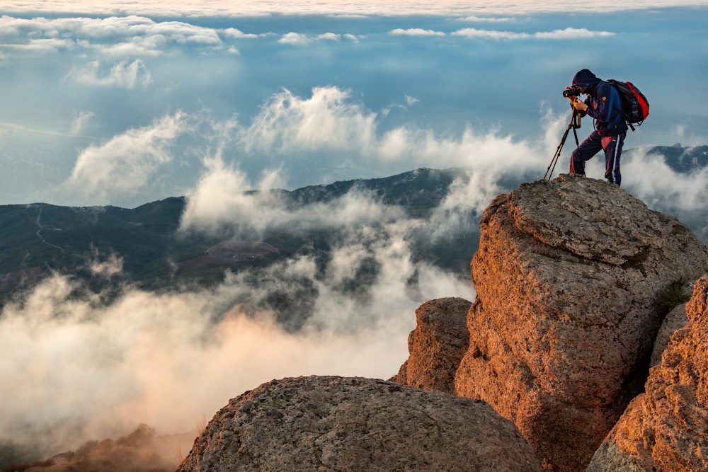 man in black jacket standing on brown rock formation under white clouds during daytime