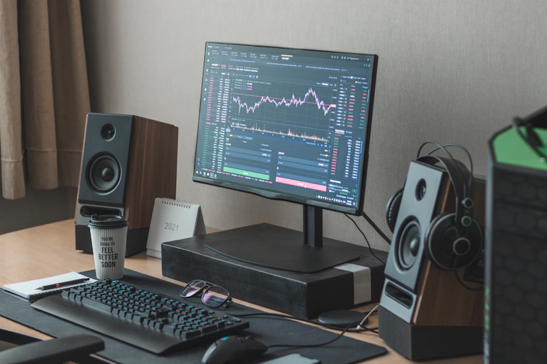 A cozy desk setup with a laptop displaying trading charts, a notebook filled with handwritten notes, and a cup of coffee steaming beside it.