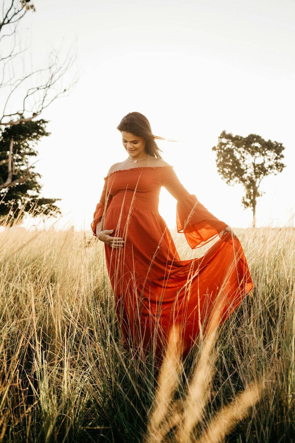 femme en robe orange debout sur le champ d’herbe pendant la journée