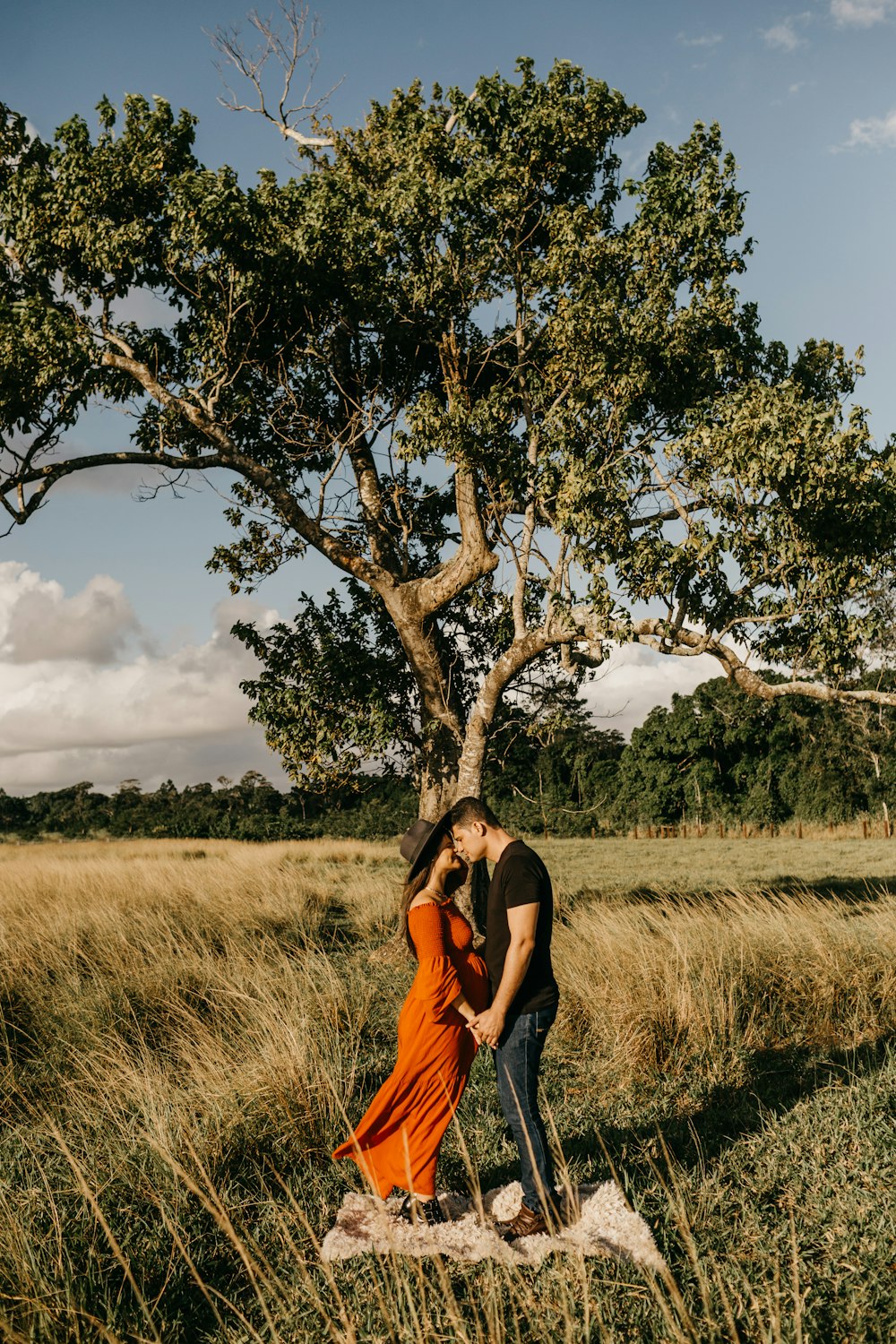 woman in orange sleeveless dress standing beside brown tree during daytime