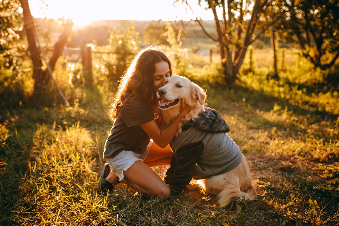 woman in black shirt sitting on brown grass field with white short coated dog during daytime