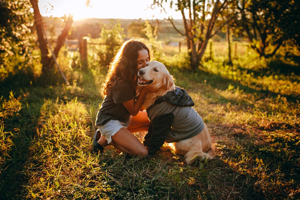 Donna in maglietta nera e pantaloncini marroni seduta sul campo di erba marrone con cane bianco