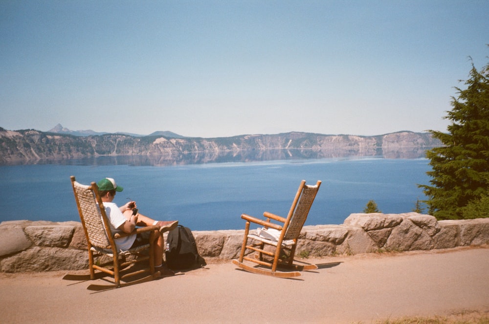 2 사람 동안 수역 근처의 갈색 모래 위에 갈색 나무 흔들 의자에 앉아