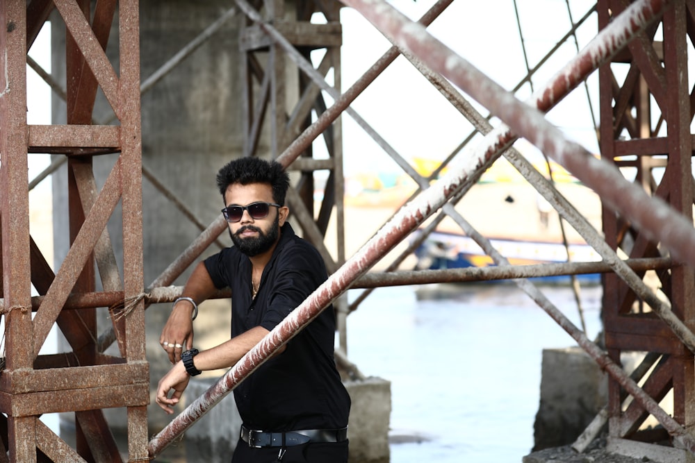 man in black crew neck t-shirt wearing black sunglasses standing on bridge during daytime