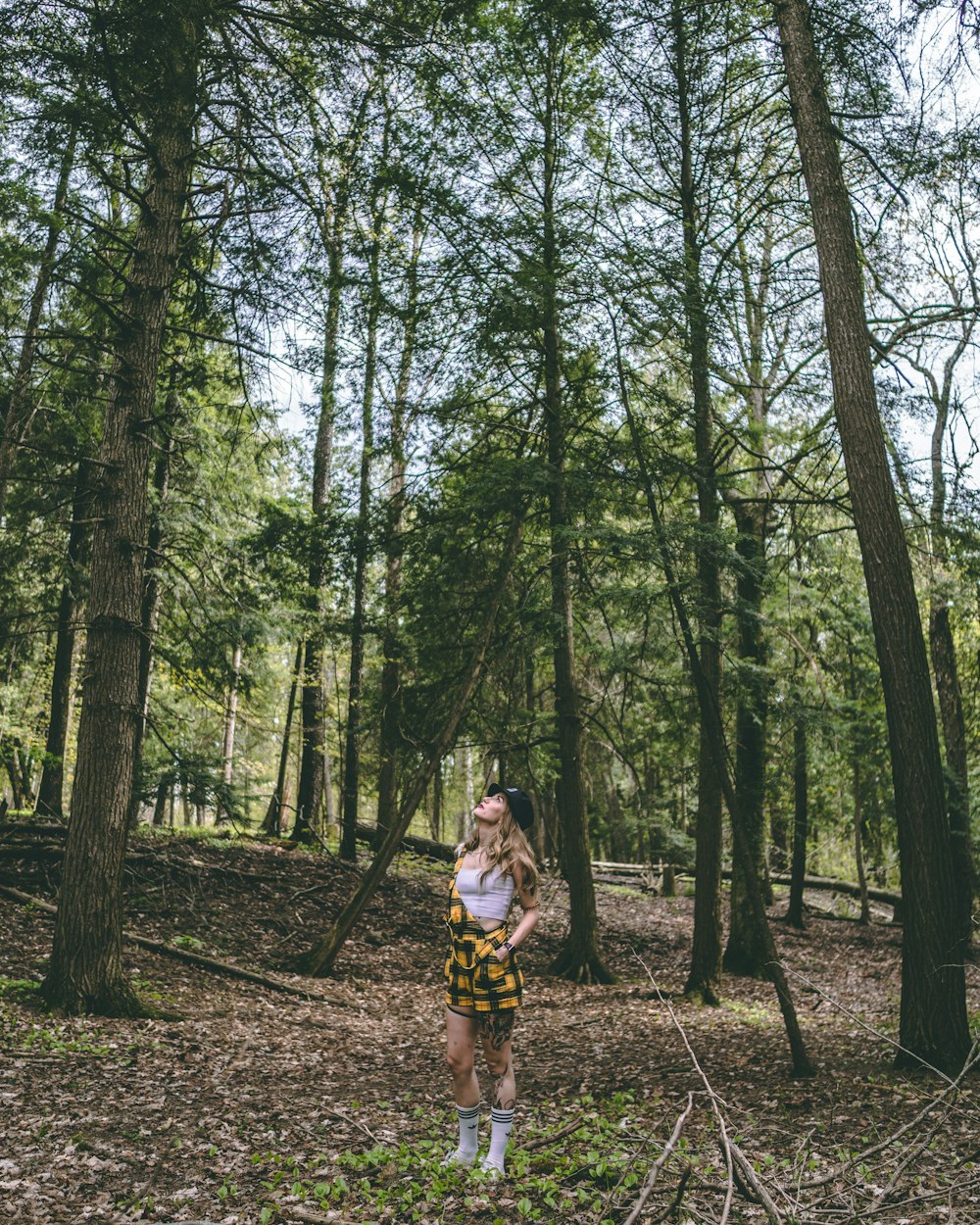 woman in white t-shirt and yellow shorts standing on forest during daytime