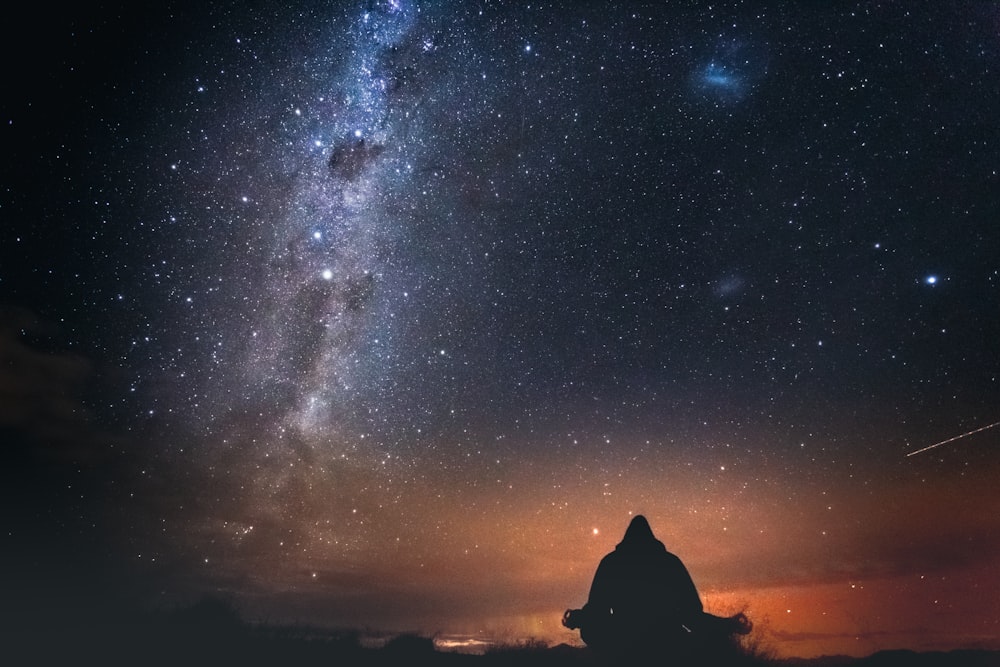 silhouette of person sitting on rock under starry night