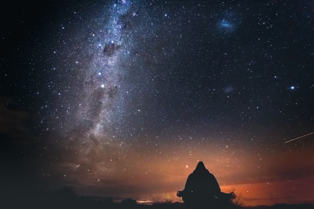 silueta de una persona sentada en una roca bajo la noche estrellada