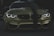 A stylish and aggressive-looking BMW car with its headlights on, displaying bold text 'FAKE TAXI' on the bumper. The car features a sleek, shiny surface with a dark green stripe running down the center of the hood and is set against a dimly lit background.