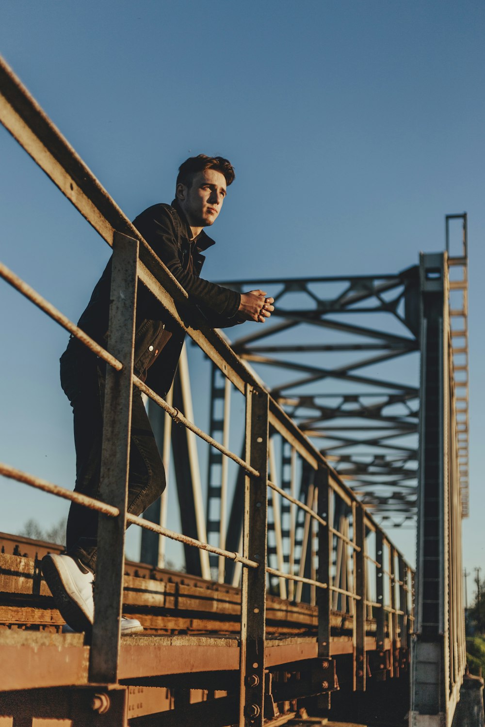 man in black jacket standing on brown metal railings during daytime