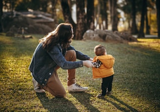 woman in blue denim jacket carrying child in blue jacket on green grass field during daytime