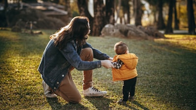 woman in blue denim jacket carrying child in blue jacket on green grass field during daytime
