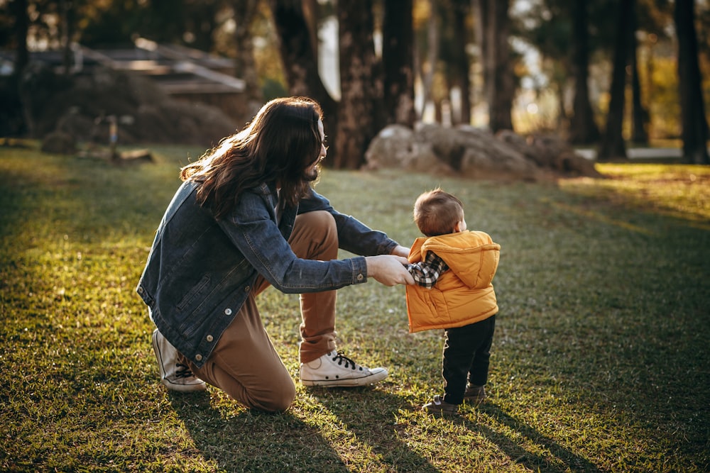 woman in blue denim jacket carrying child in blue jacket on green grass field during daytime