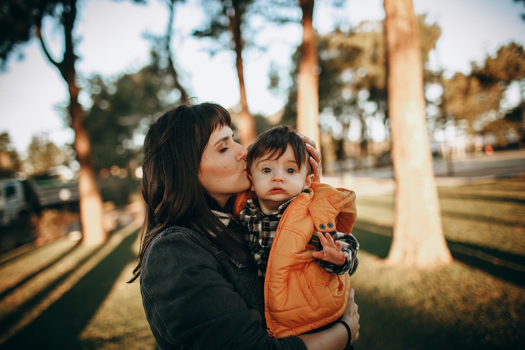 woman in black jacket carrying baby in orange jacket