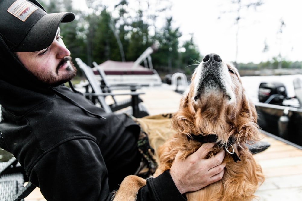 man in black jacket holding brown long coated dog