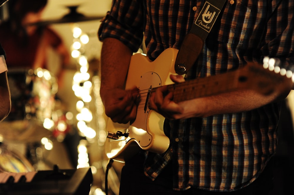 man in black and white checkered button up shirt playing white electric guitar