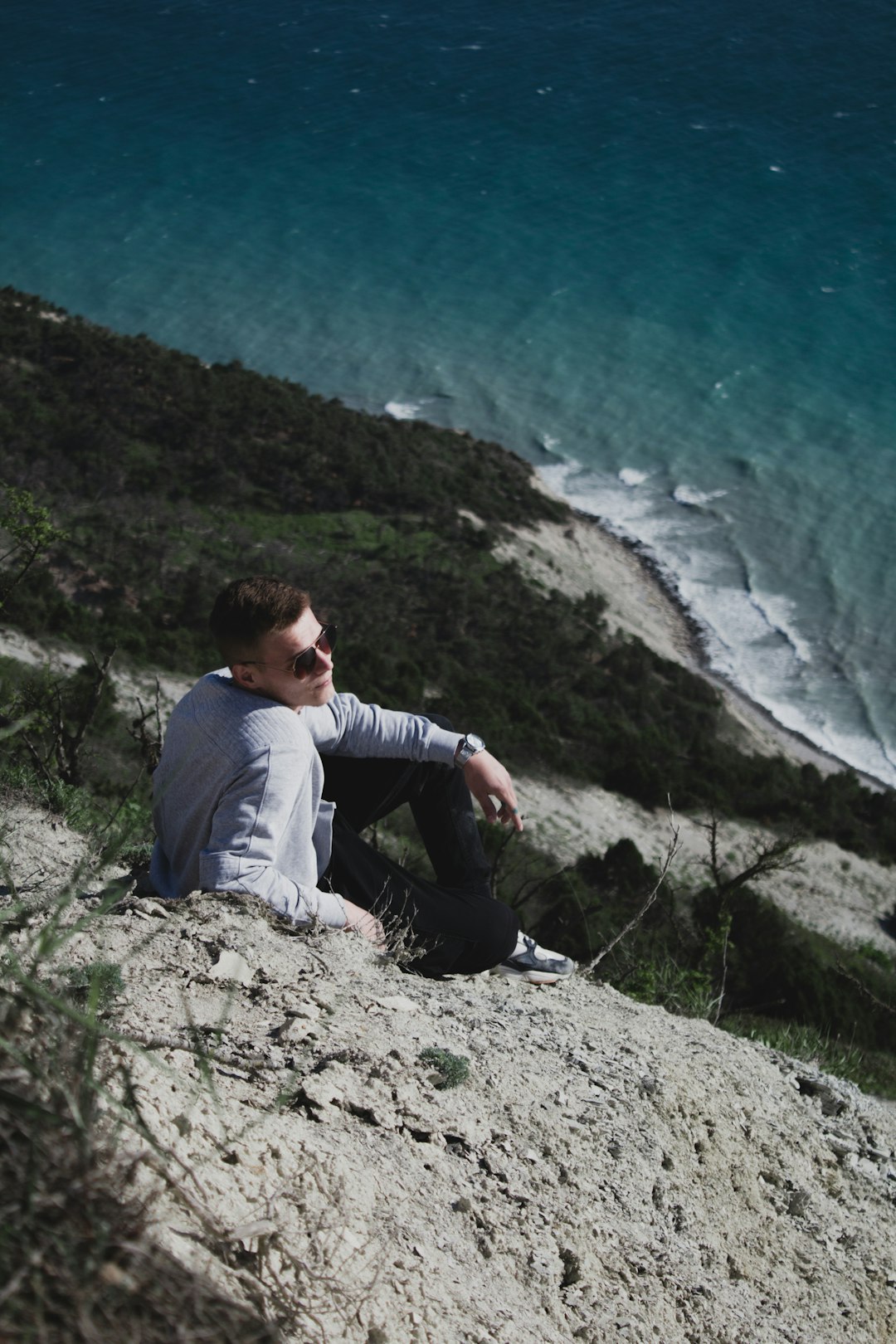 man in gray long sleeve shirt sitting on rock near body of water during daytime