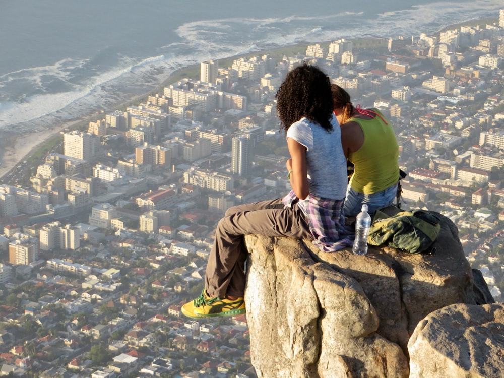 woman in blue t-shirt and brown pants sitting on rock during daytime