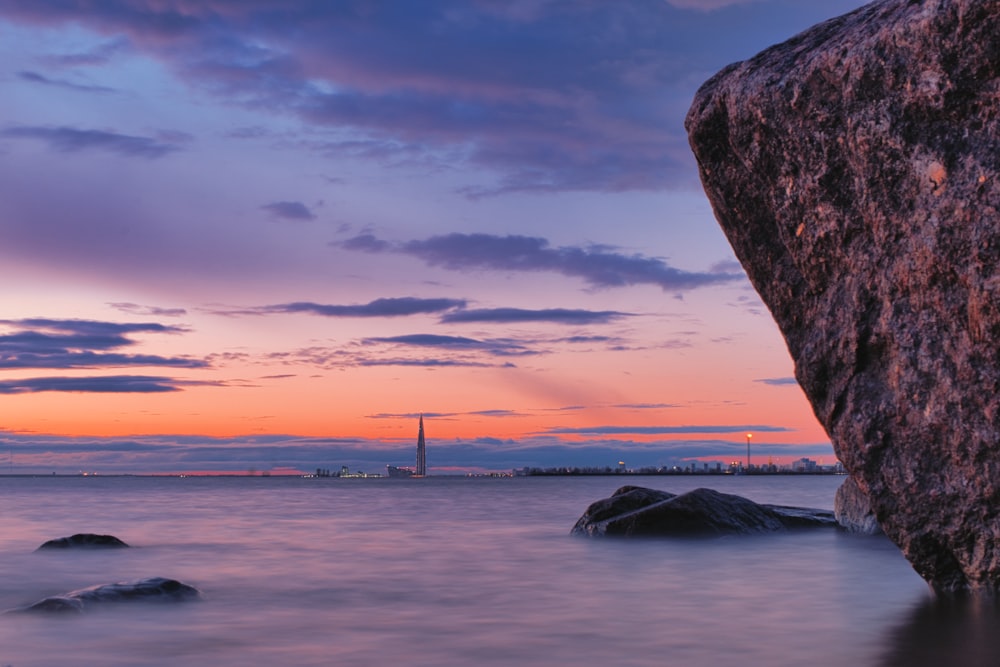 body of water near brown rock formation during sunset