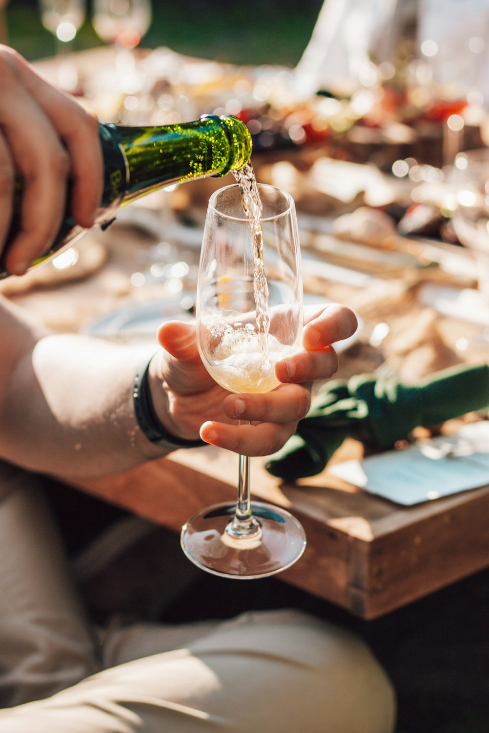 person holding green glass bottle pouring on clear wine glass