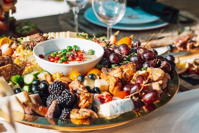 A vibrant grazing table set outdoors with colorful seasonal fruits, vegetables, cheeses, and homemade breads arranged invitingly.