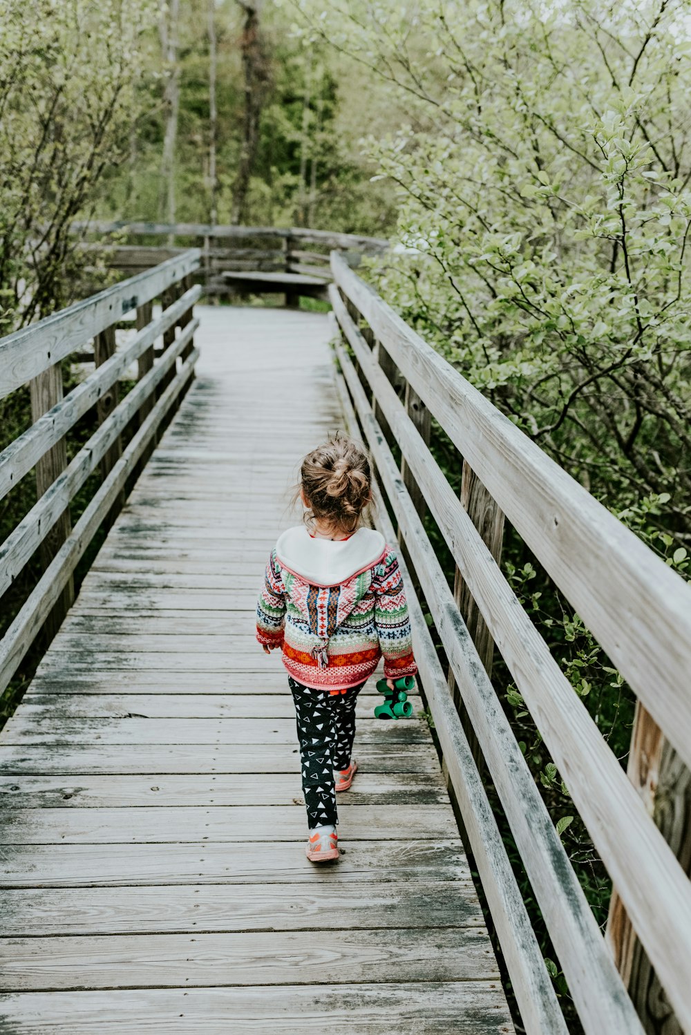 girl in white and red long sleeve shirt standing on wooden bridge