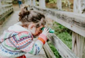 girl in white and red sweater leaning on brown wooden fence during daytime