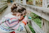 girl in white and red sweater leaning on brown wooden fence during daytime