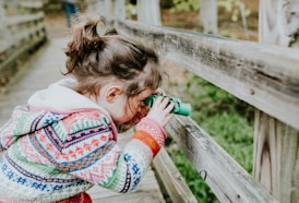 girl in white and red sweater leaning on brown wooden fence during daytime