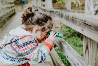 girl in white and red sweater leaning on brown wooden fence during daytime
