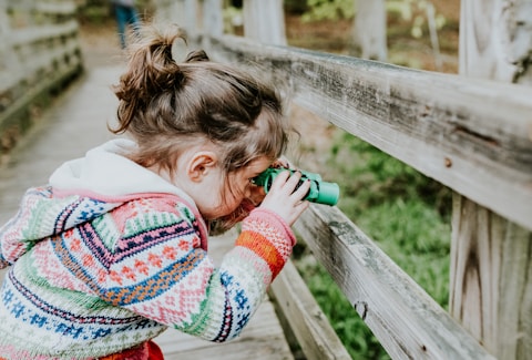 girl in white and red sweater leaning on brown wooden fence during daytime
