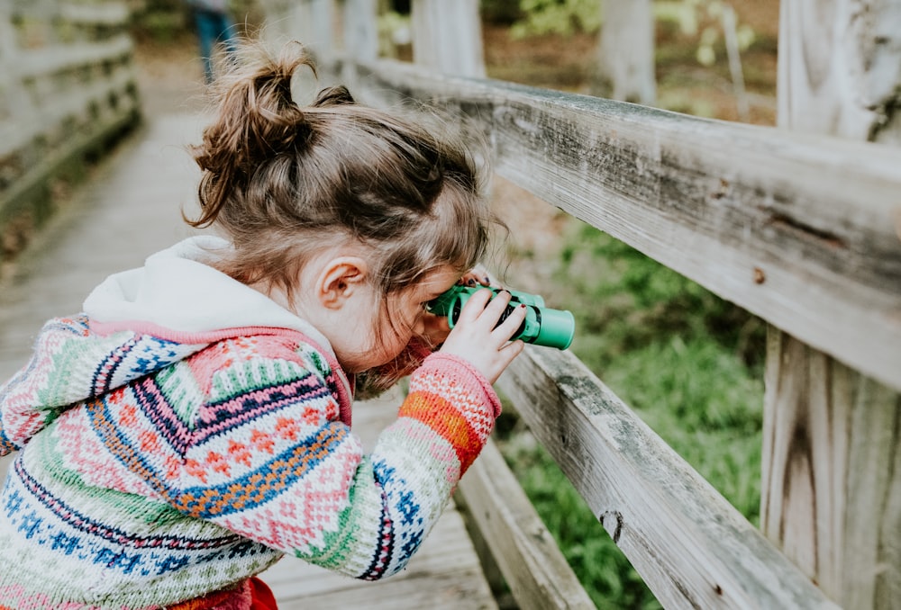 girl in white and red sweater leaning on brown wooden fence during daytime