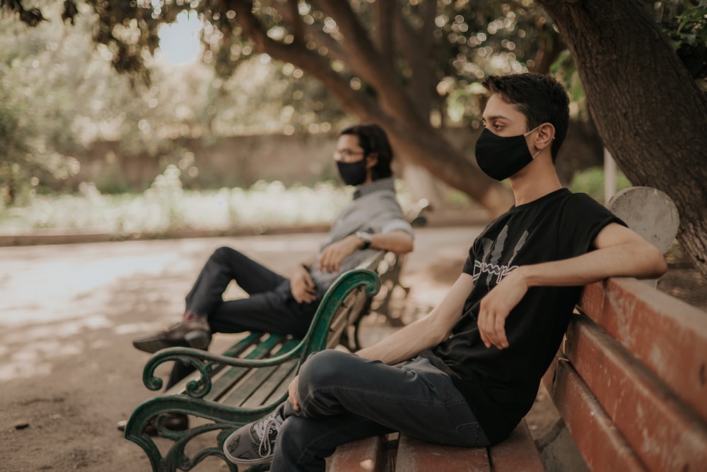 homme en noir ras du cou T-shirt assis sur un banc vert pendant la journée