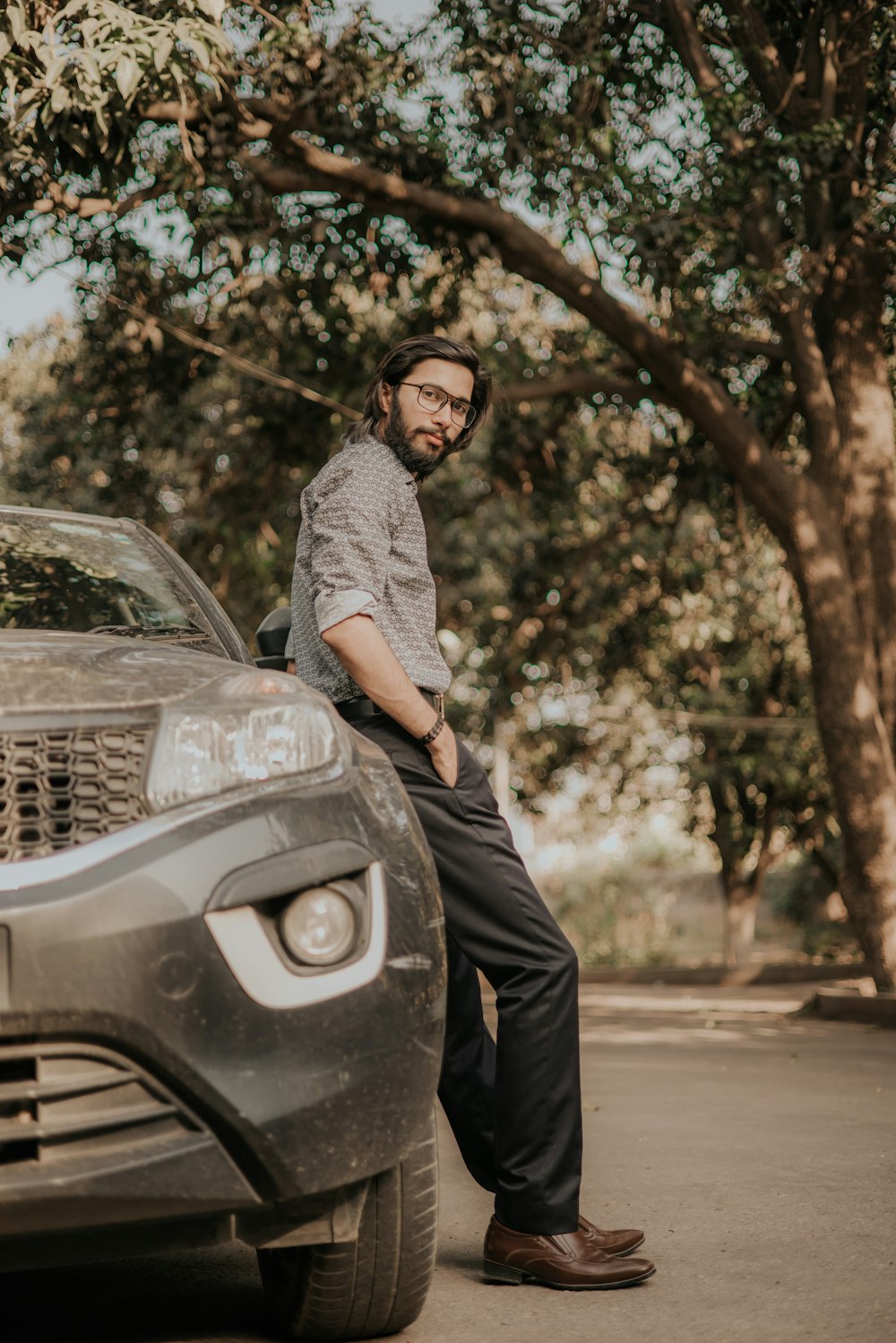 man in grey dress shirt and black pants sitting on black car